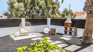 A rooftop garden with a seating area, a grill, and a decorative tree stump.