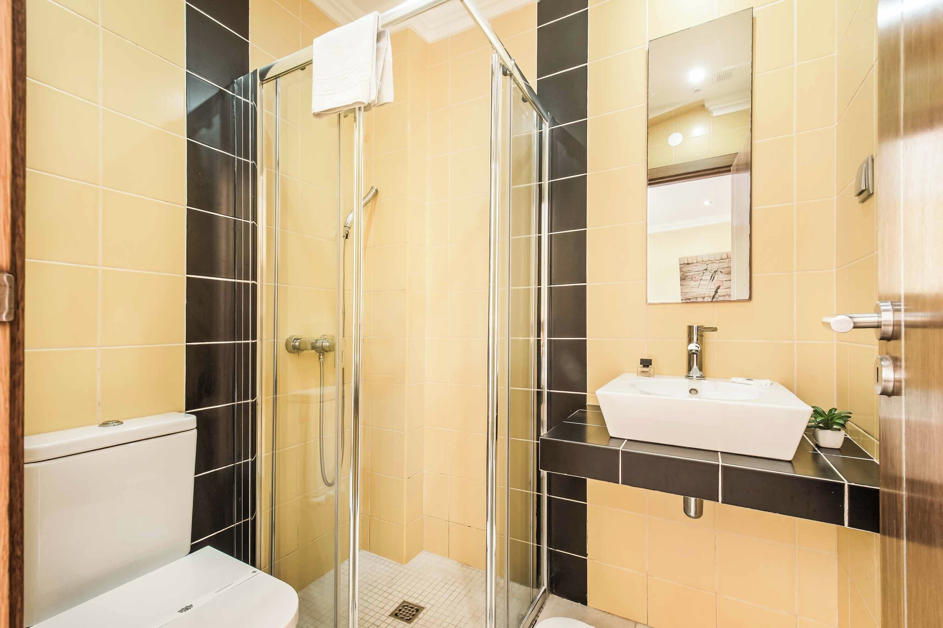 Ein modernes Badezimmer mit einer Glaskabine zur Dusche, einem weißen Waschbecken und einem Spiegel darüber.