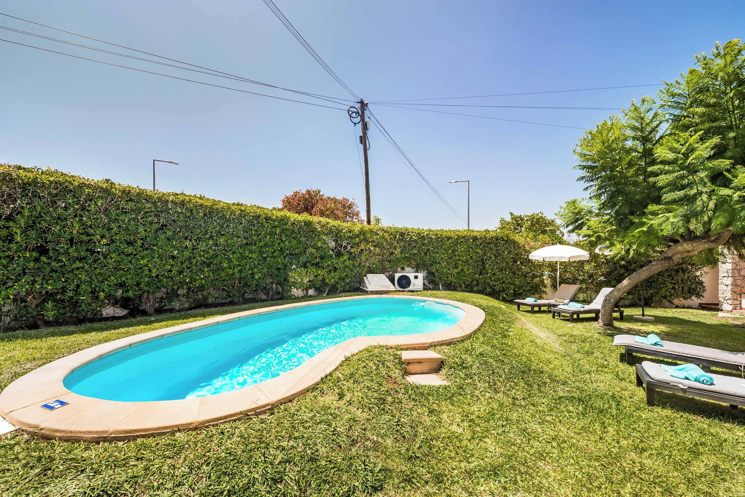 A swimming pool with a curved edge, surrounded by well-maintained grass and a hedge.