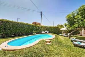 A swimming pool with a curved edge, surrounded by well-maintained grass and a hedge. - Villa Sueste - Two Bedroom Villa, Sleeps 4 (Albufeira)