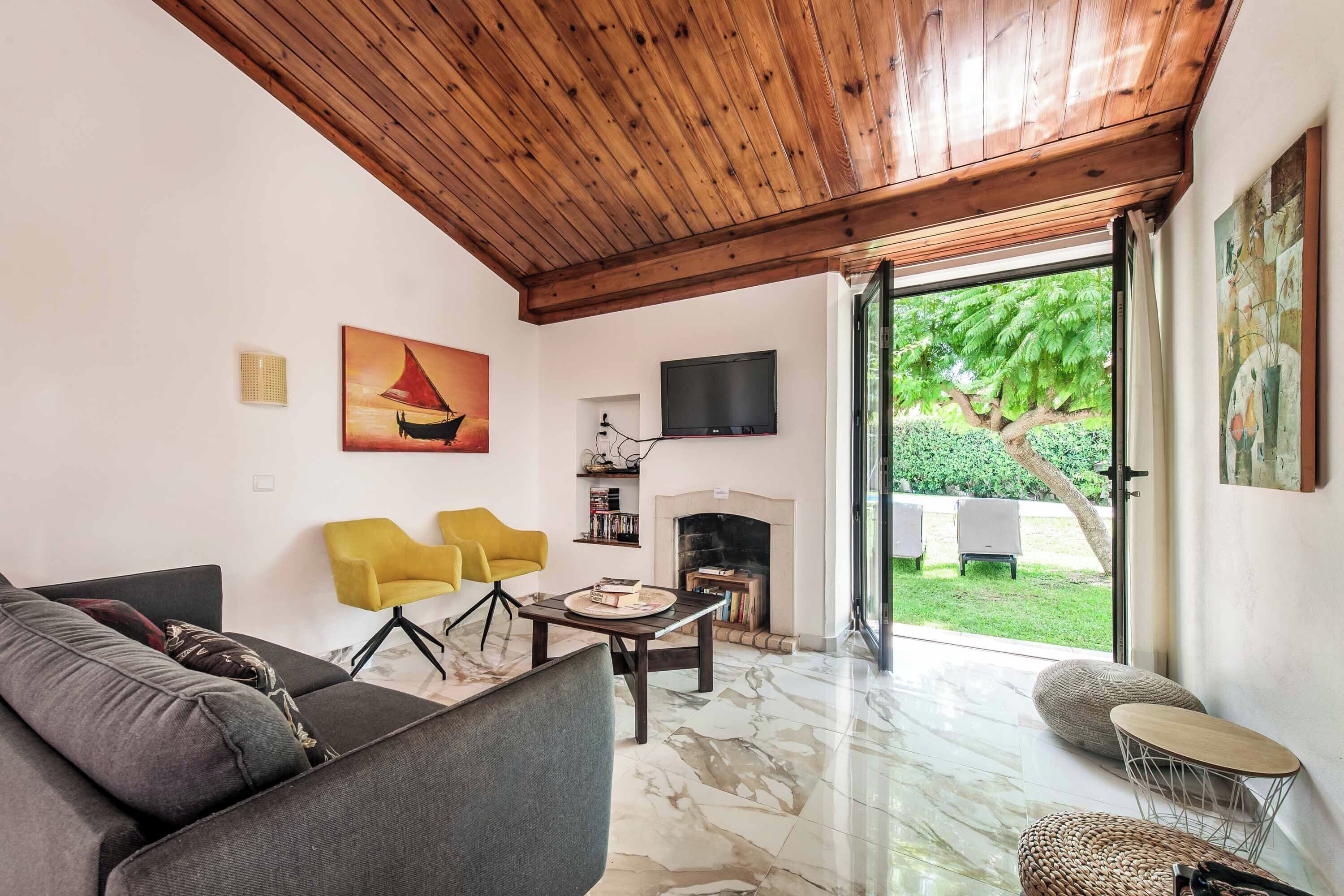 Un salon avec un canapé, deux fauteuils jaunes, une cheminée, un téléviseur et un tableau.