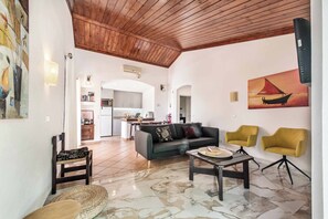 A spacious living area with a wooden ceiling, a kitchen in the background, and a dining area with yellow chairs. - Villa Sueste - Two Bedroom Villa, Sleeps 4 (Albufeira)
