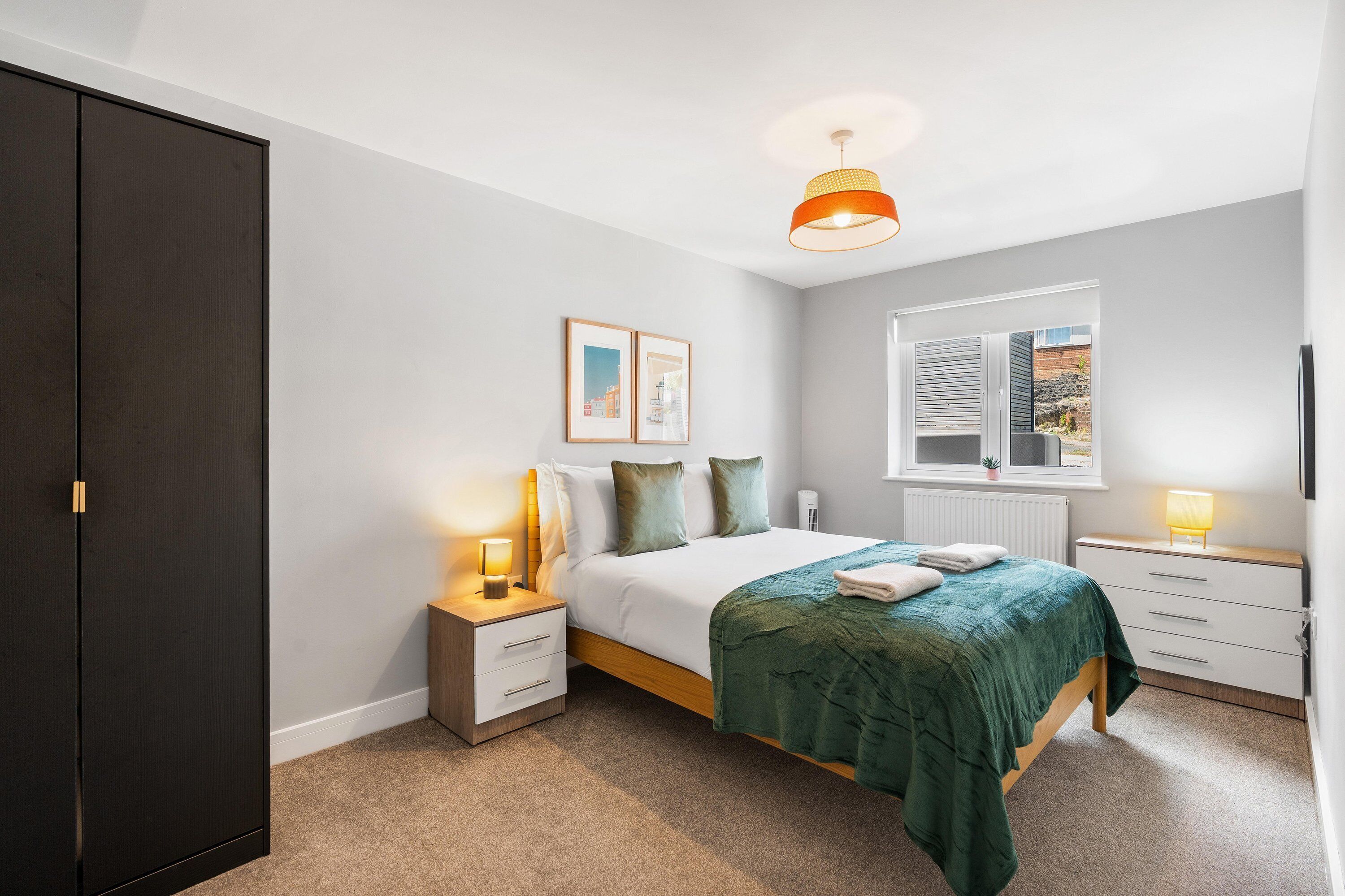 A bedroom with a bed, bedside tables, a wardrobe, a window, and a hanging light fixture.