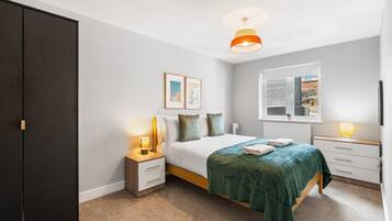 A bedroom with a bed, bedside tables, a wardrobe, a window, and a hanging light fixture.