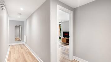 A hallway with a wooden floor, a white door leading to a room with a television, and a radiator on the wall.
