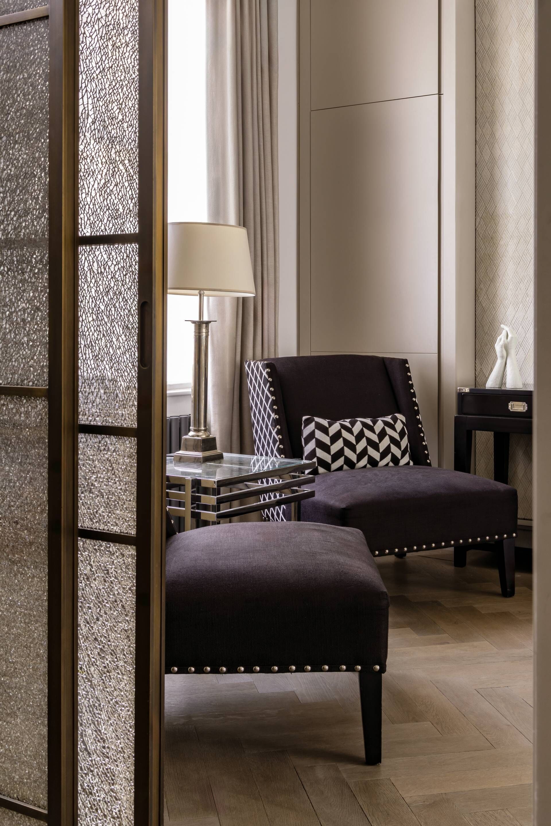 A modern living room with a sofa, ottoman, and a side table with a lamp.