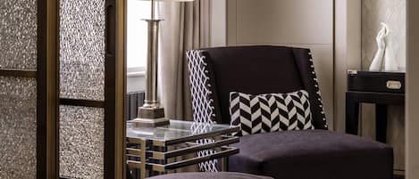 A modern living room with a sofa, ottoman, and a side table with a lamp.