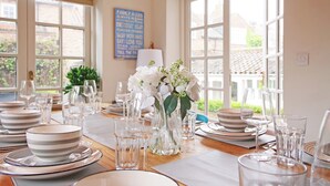 Ein Esszimmer mit gedecktem Tisch, klarem Geschirr und Gläsern, einer Vase mit weißen Blumen und einem Schild mit der Aufschrift 'Familienregeln' an der Wand.
