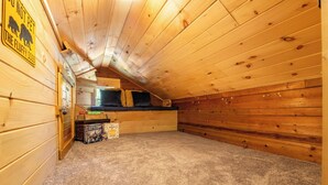 Um quarto de sótão com piso carpido, teto inclinado e uma pequena janela.