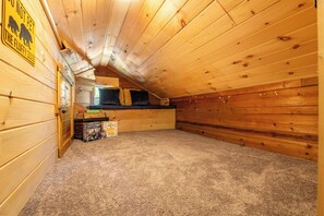 Ein Dachzimmer aus Holz mit schrägem Dach, Teppichboden und einem kleinen Fenster.