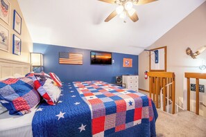Ein Schlafzimmer mit einem Bett, einem Deckenventilator, einer Flagge und einer Tür zu einem anderen Raum.