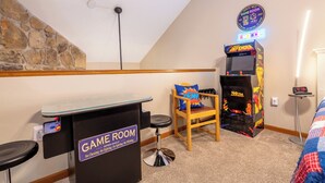 Una sala giochi con parete in pietra, insegna luminosa al neon, console di gioco, una sedia e un orologio.