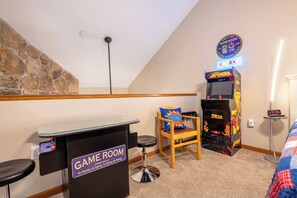 Ein Spielzimmer mit Steinwand, einer Neonreklame, einer Spielkonsole, einem Sessel und einer Uhr.