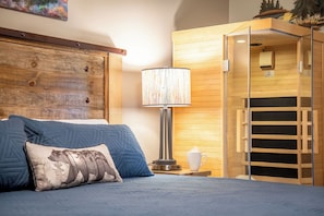 Een slaapkamer met een bed, nachtkastje, lamp en een houten garderobe.