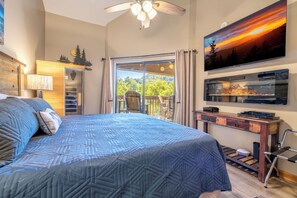 Ein Schlafzimmer mit einem großen Bett, einem Deckenventilator, einem Fernseher und Blick ins Freie.