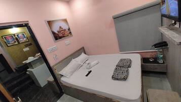 Habitación de hotel con cama, mostrador de recepción, un cuadro en la pared y una mesita con una botella y vasos.