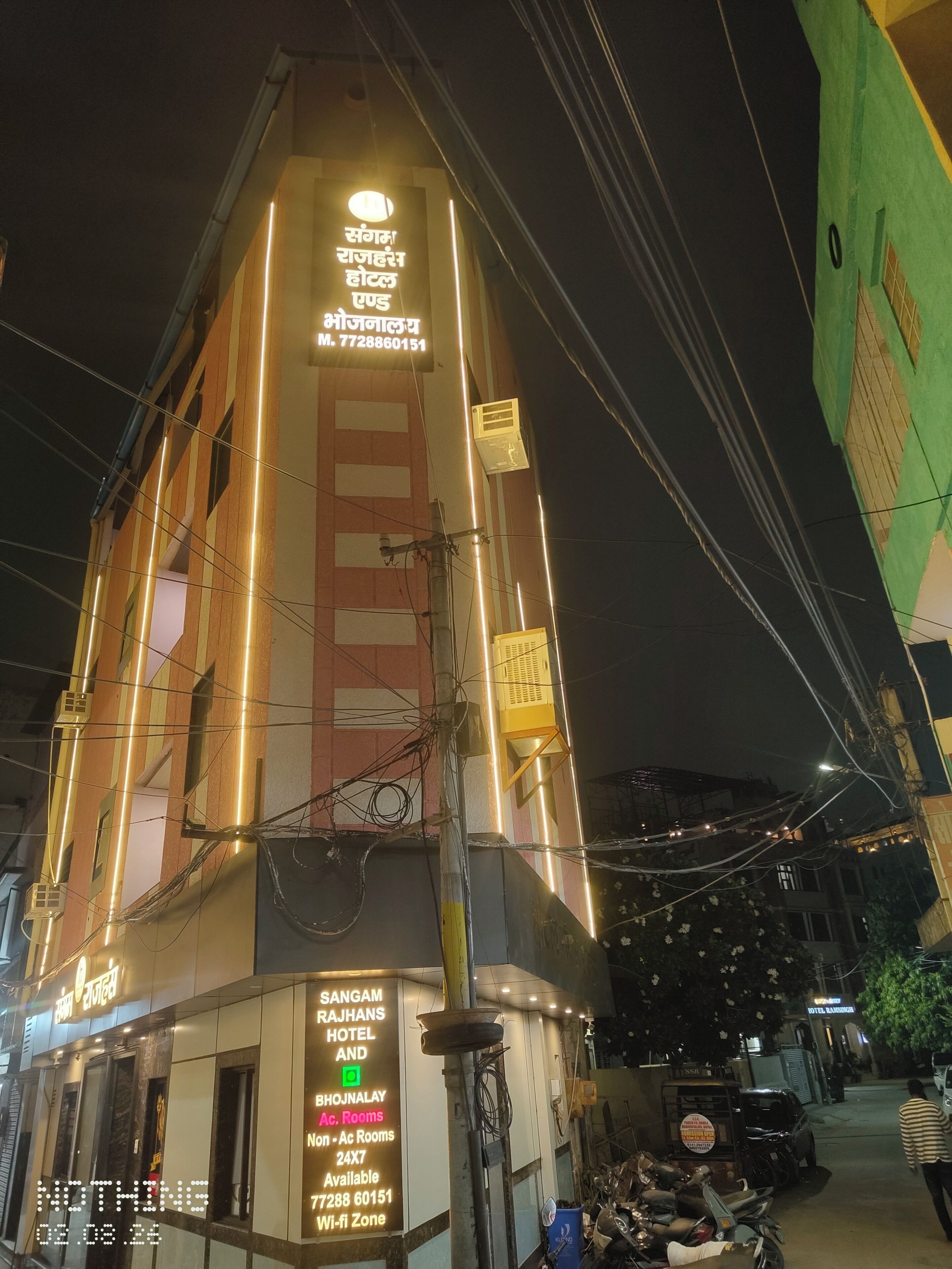 Un hotel con un cartel que indica 'Sangam Rajahans Hotel and Bhujanalay Ac. Rooms' y un número de contacto.