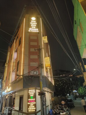 Een hotel met een bord waarop 'Sangam Rajahans Hotel and Bhujanalay Ac. Rooms' en een contactnummer staan.