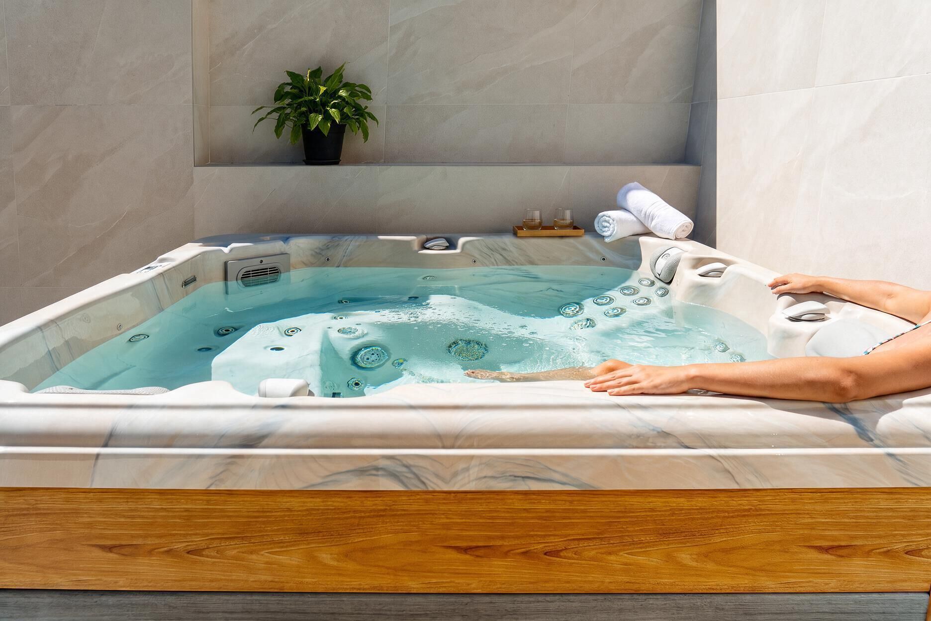 Una persona relajándose en un jacuzzi con una planta y toallas a un lado.