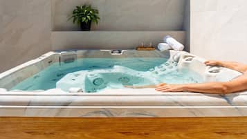 Una persona relajándose en un jacuzzi con una planta y toallas a un lado.