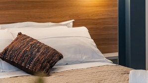 Una cama bien hecha con un cojín texturizado, un cojín blanco y una manta color beige.