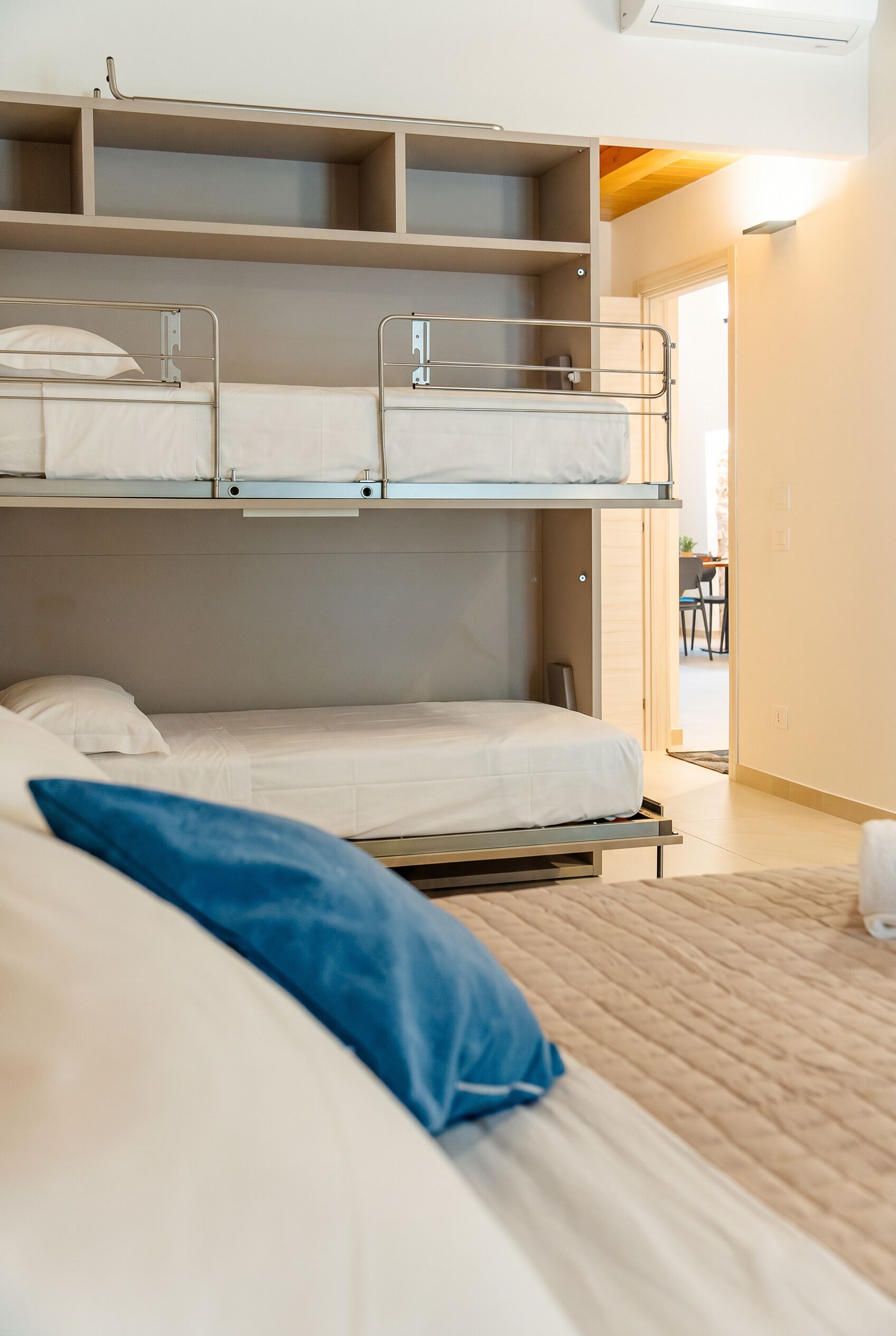 A bunk bed room with a wooden floor, a door leading to a dining area, and a ceiling fan.
