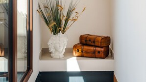 Un reloj de pared, un jarrón decorativo con plantas secas y dos maletas de estilo antiguo sobre una estantería.