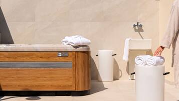 A modern bathroom with a wooden bathtub, a toilet, and a towel dispenser.