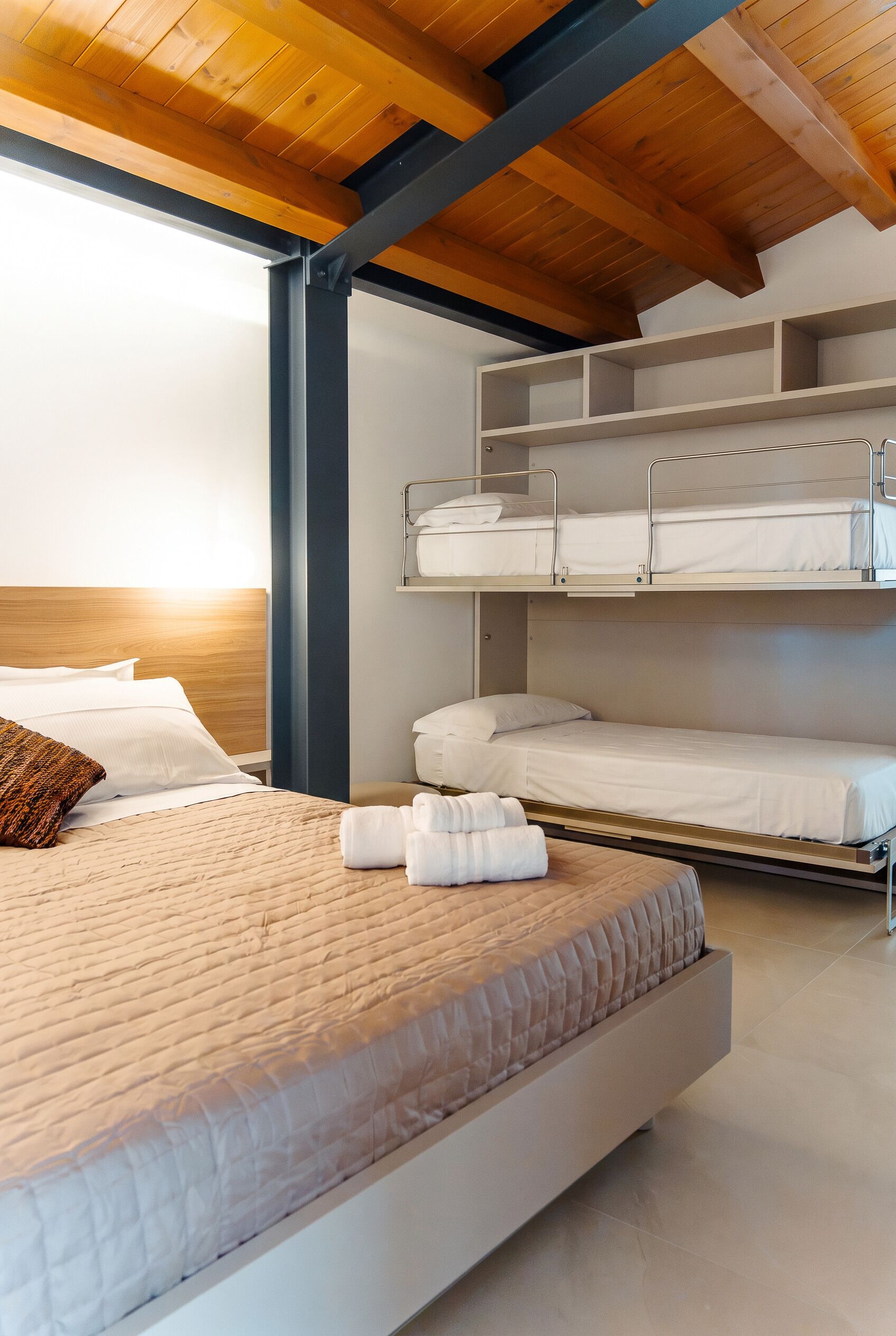 A hotel room with a bunk bed, a single bed, and a wooden ceiling.