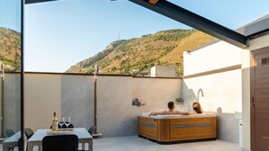Un área de spa con una bañera de hidromasaje, una mesa con copas de vino y una botella, y vistas a un paisaje montañoso.