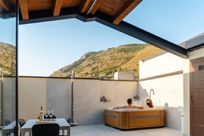 A spa area with a hot tub, a table with wine glasses and a bottle, and a view of a hilly landscape.