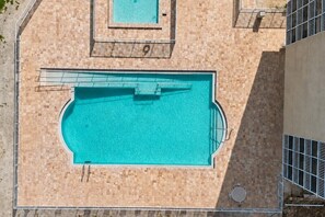 Eine Vogelperspektive auf einen Swimmingpool mit Fliesen umrandet, einem Sprungturm und einem kleinen, runden Pool.