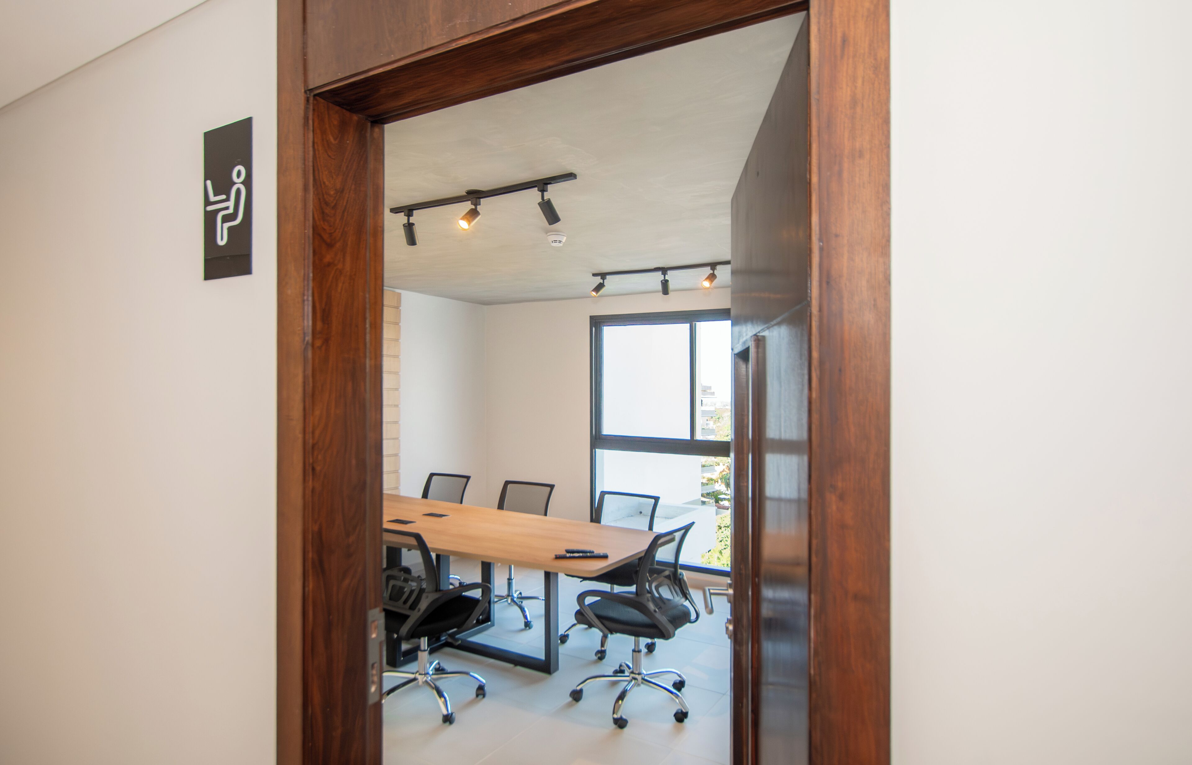 A conference room with a wooden table, black office chairs, and a large window providing natural light.