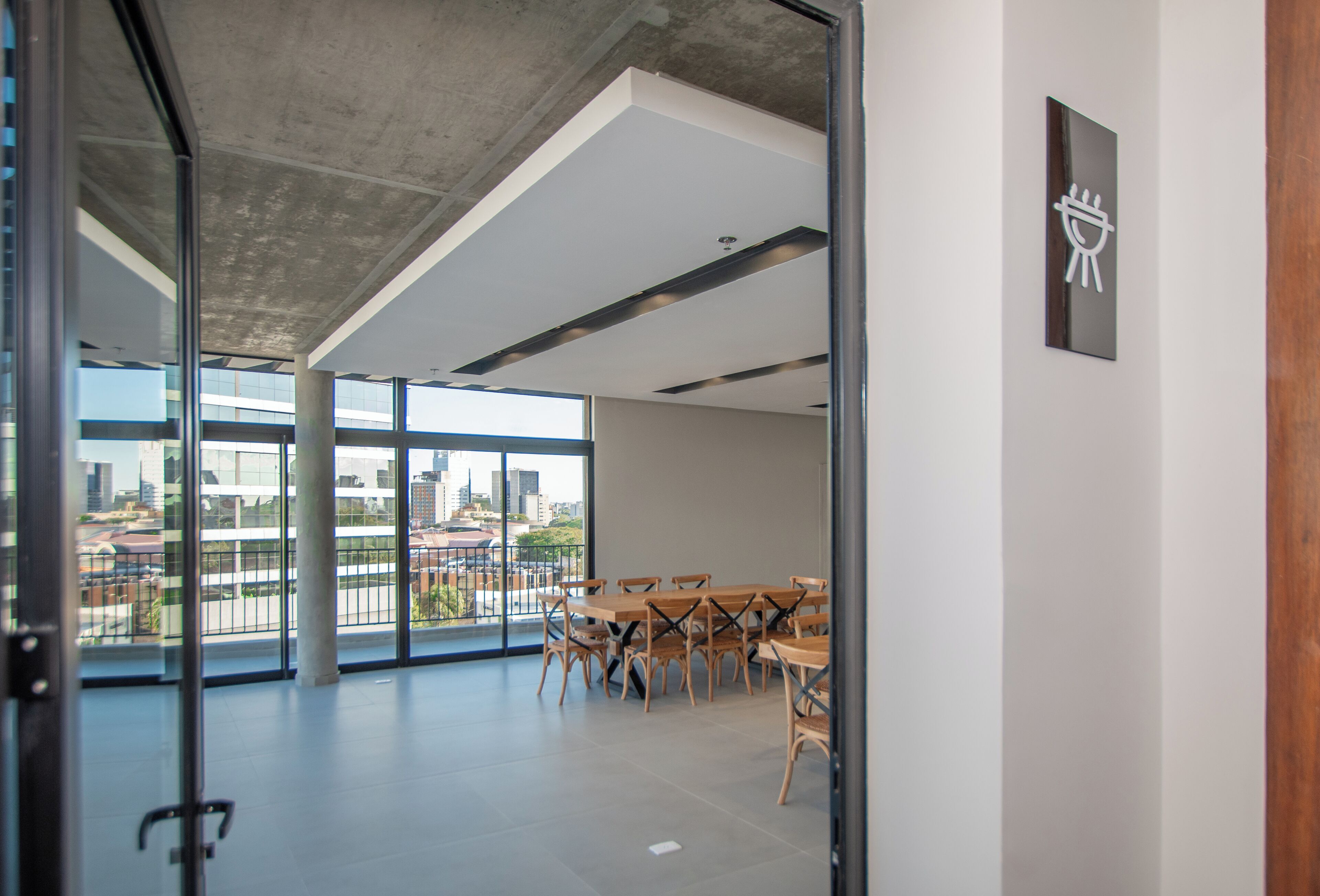 An interior space with a conference table and chairs, large windows with a city view, and a concrete ceiling.