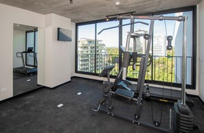 A gym with exercise equipment, a treadmill, and a large window with a city view. - Corporate Stays First del Sol - 201 (Asunción)