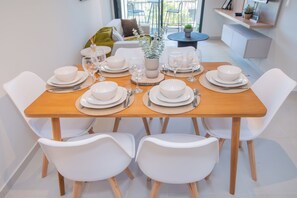 Ein Esstisch mit weißen Tellern, Schüsseln und Besteck, umgeben von weißen Stühlen in einem modernen Interieur.