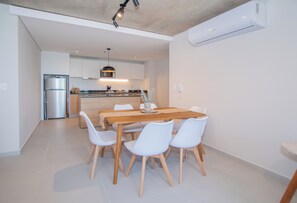 A modern kitchen with a dining area, white chairs, and a wooden table. - Corporate Stays First del Sol - 201 (Asunción)