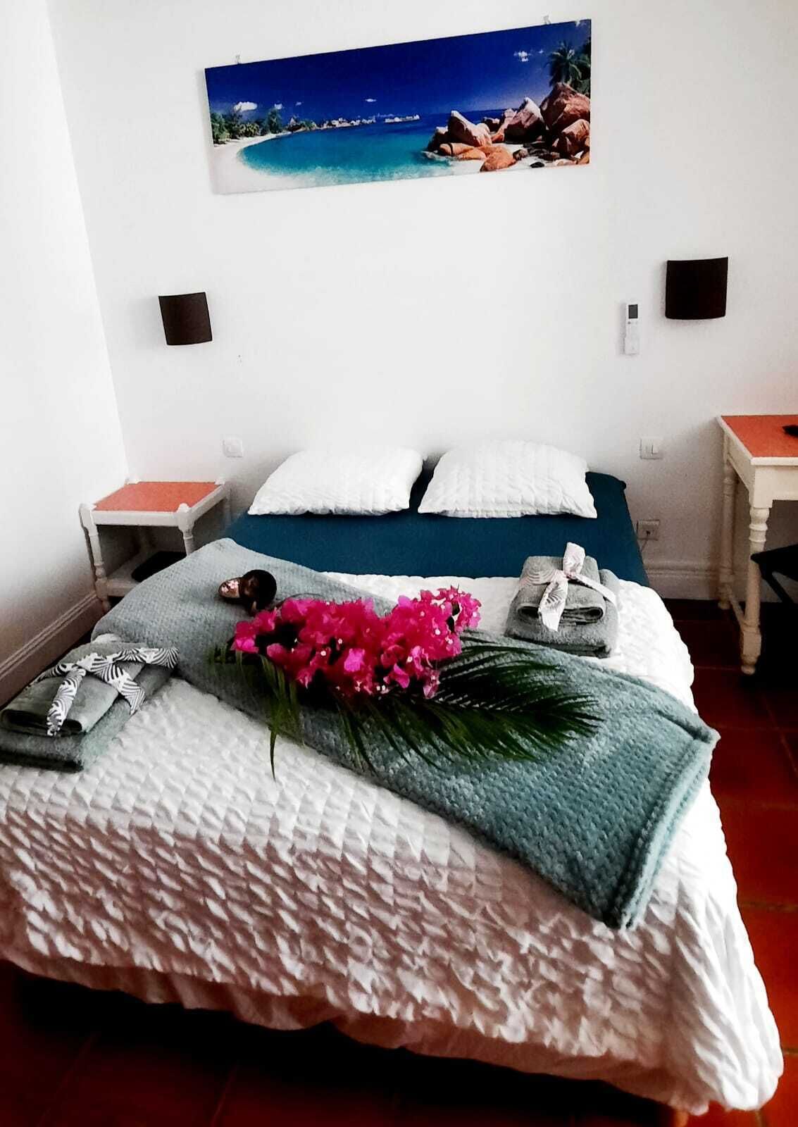 A neatly made bed with a blue headboard, white pillows, and a decorative arrangement including a pink flower and a green plant.
