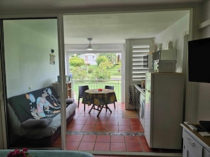 A room with a sliding glass door leading to a balcony, a dining table with chairs, a sofa, a washing machine, and a television.