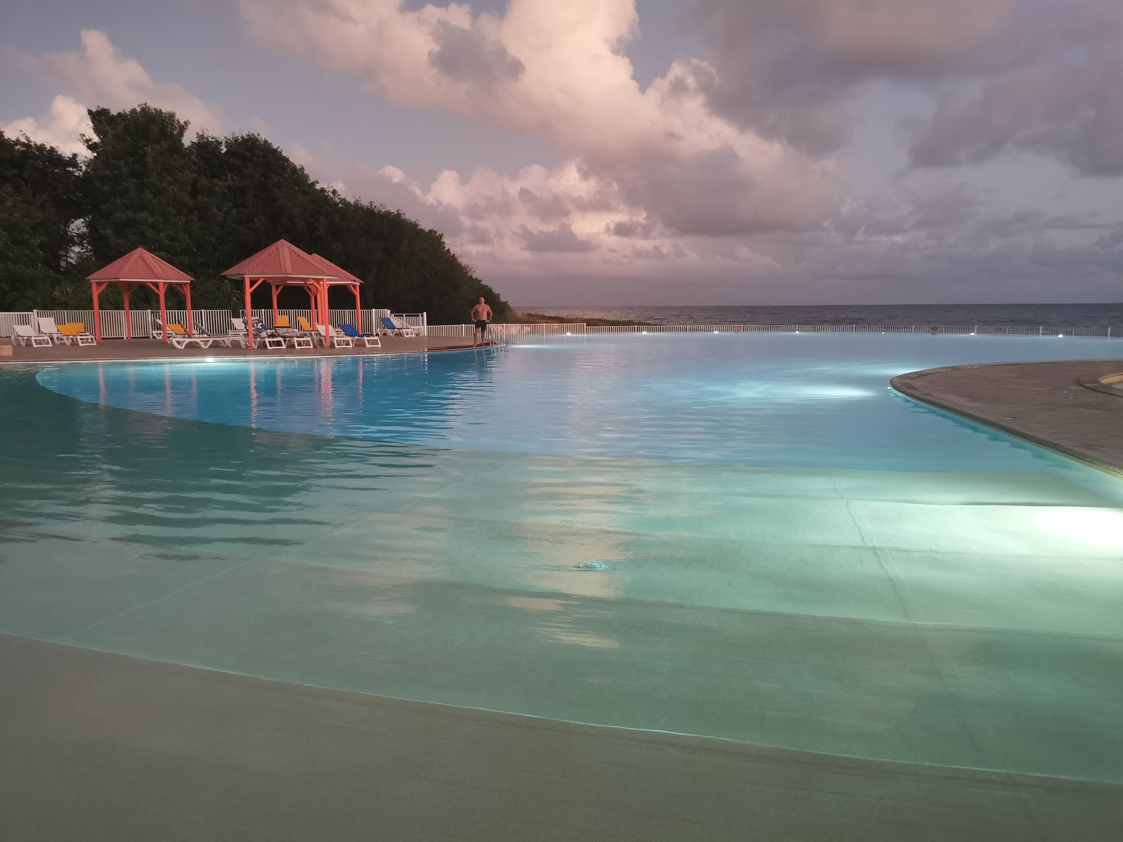 A swimming pool with lounge chairs and a gazebo, surrounded by a beach and ocean view.