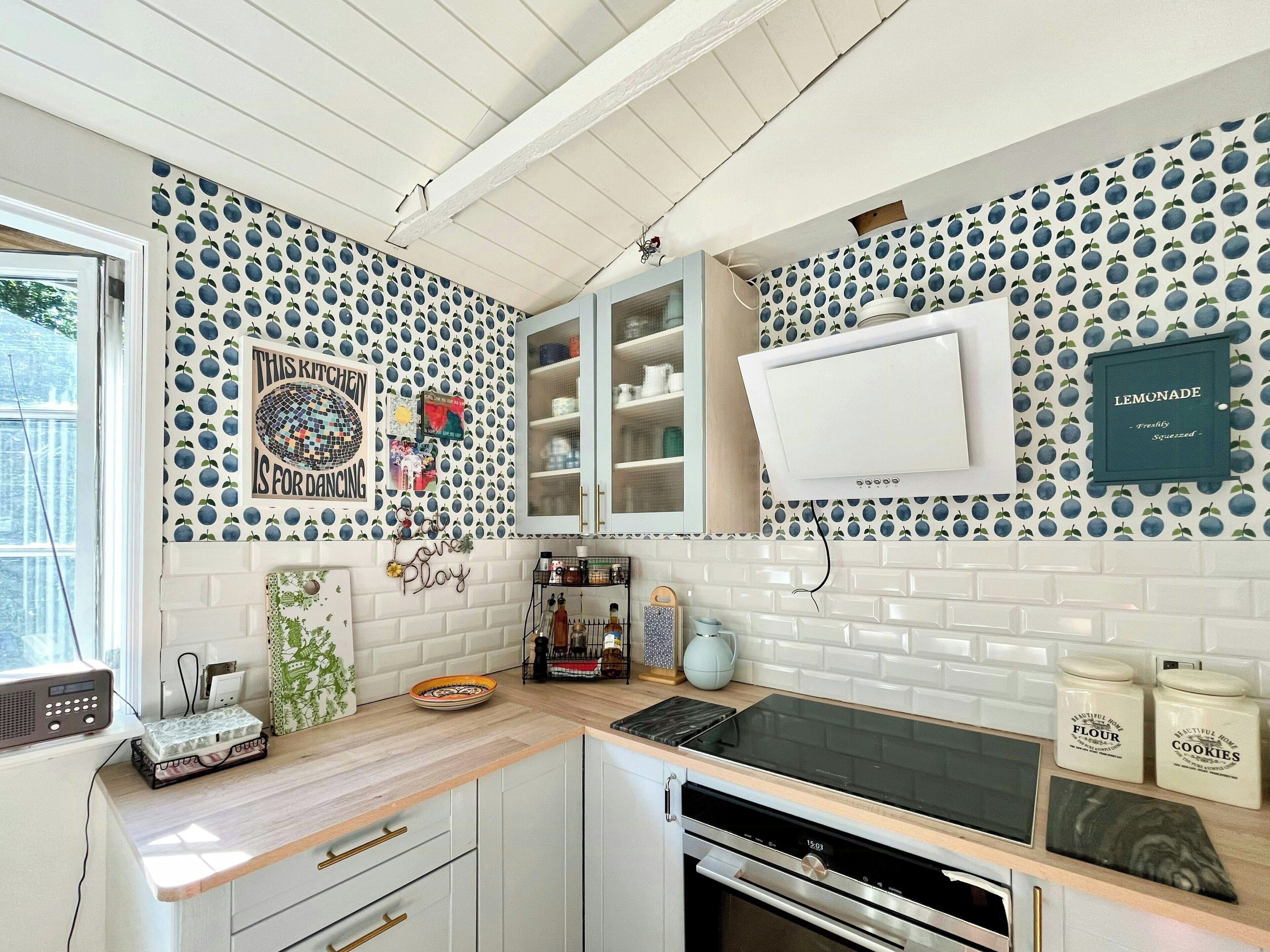 Cocina con armarios blancos, estufa negra y microondas. Se ve una ventana con vistas a árboles.