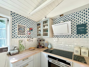 A kitchen with white cabinets, a black stove, and a microwave. There is a window with a view of trees. - Stay in" Sandersvig delight" filled with colours (Haderslev)