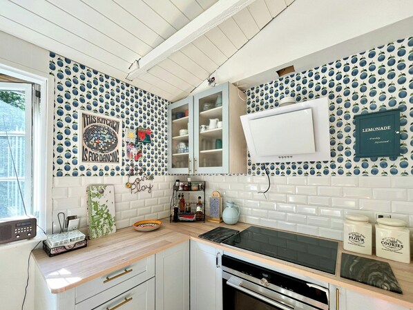 A kitchen with white cabinets, a black stove, and a microwave. There is a window with a view of trees. - Stay in" Sandersvig delight" filled with colours (Haderslev)