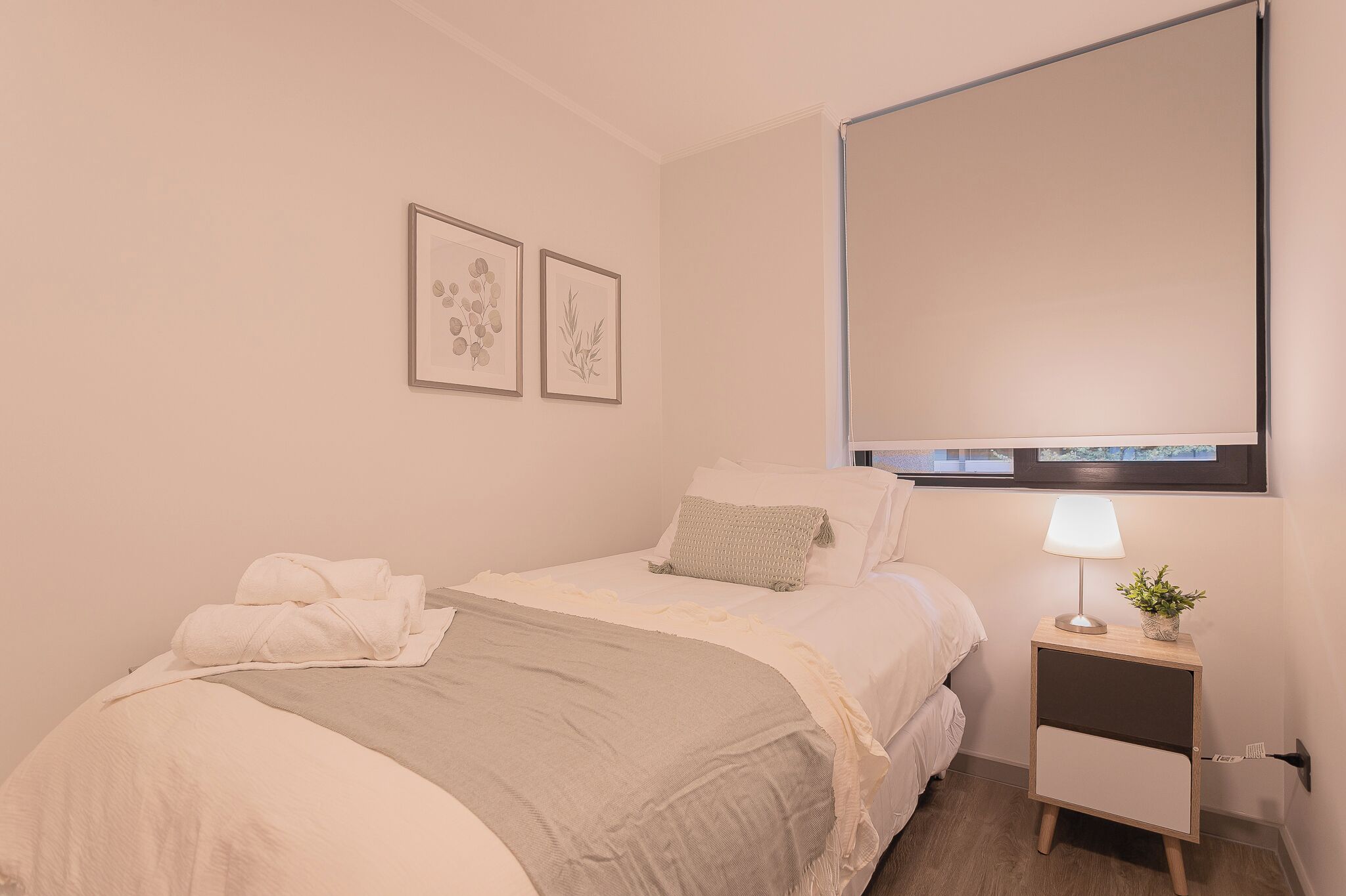 Ein Hotelzimmer mit einem Bett, einem Nachttisch mit Lampe sowie zwei gerahmten Pflanzenbildern an der Wand.