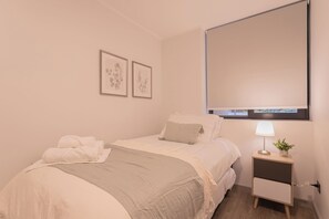 A hotel room with a bed, a bedside table with a lamp, and two framed botanical prints on the wall.