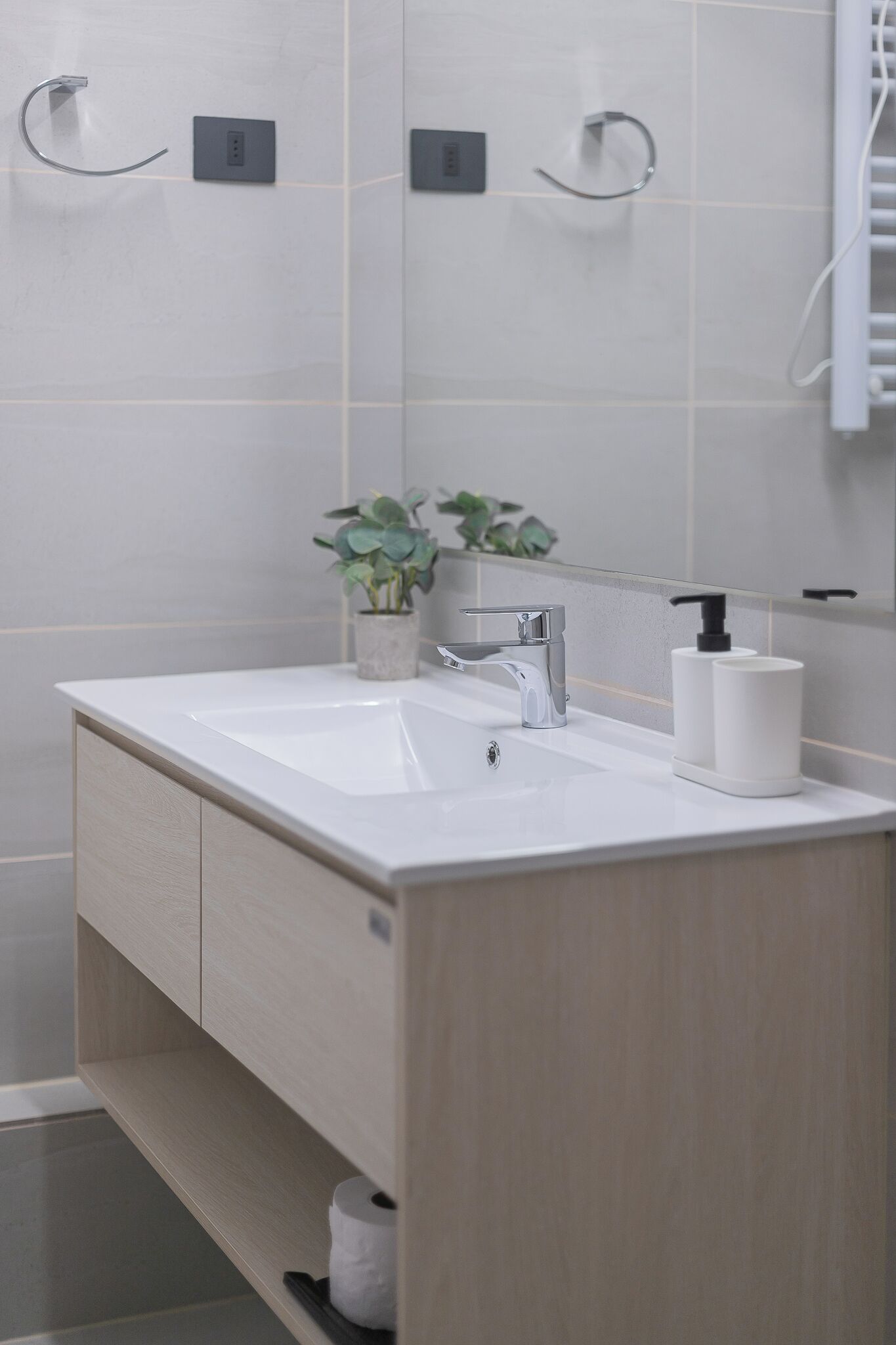 A bathroom with a white sink, a modern faucet, a soap dispenser, and a potted plant.