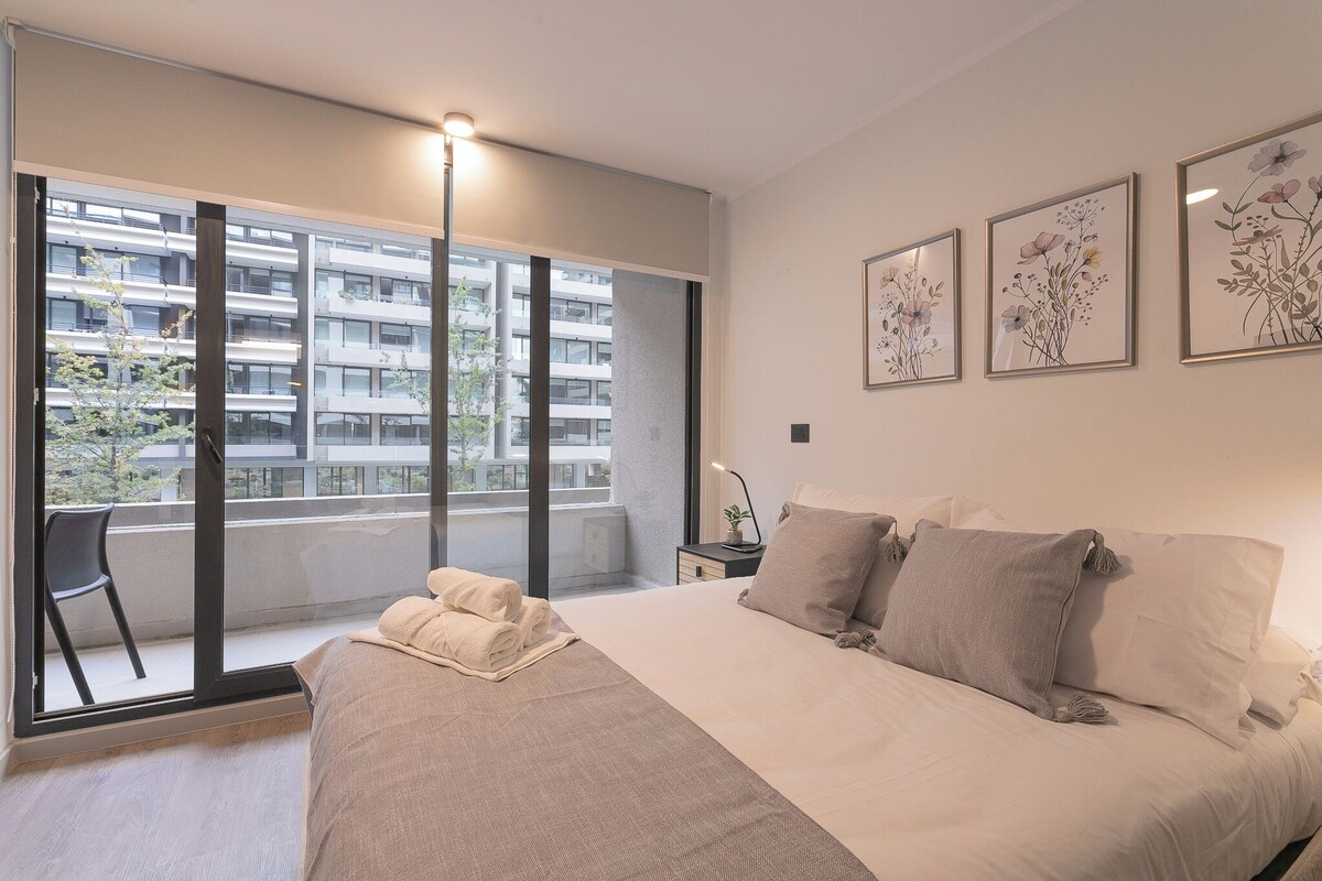 Ein modernes Schlafzimmer mit einem großen Bett, einem Sessel und einem Balkon mit Blick auf ein Gebäude.