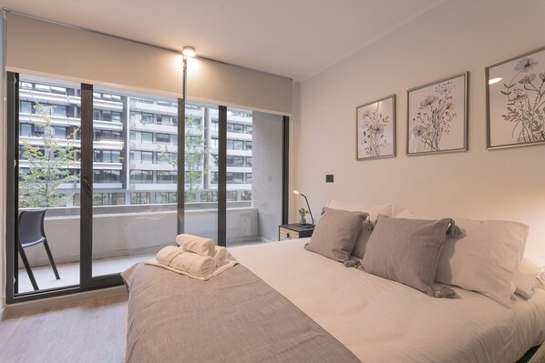 A modern bedroom with a large bed, a chair, and a balcony with a view of a building. - Pedro Valdivia Apartments by Andes STR (Providencia)