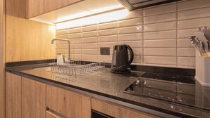 A modern kitchen with a black countertop, wooden cabinets, a stainless steel kettle, and a dish rack. - Pedro Valdivia Apartments by Andes STR (Providencia)