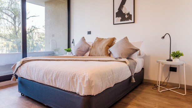 A bedroom with a bed, pillows, a bedside table, a lamp, and a window. - Pedro Valdivia Apartments by Andes STR (Providencia)